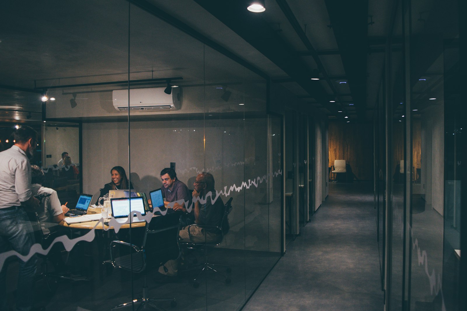 Colleagues collaborating with laptops in a glass-walled meeting room